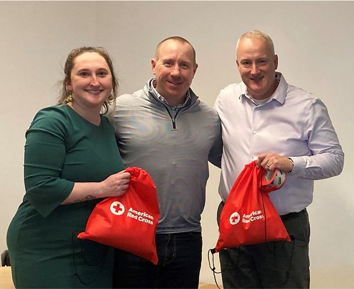 Three people holding red American Red Cross bags